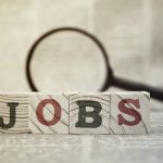 “Jobs” on wooden block and magnifying glass on newspaper background
