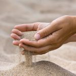 sand running through hands of woman