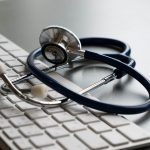 Silver stethoscope lying down on an laptop, toned blue
